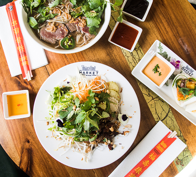 Scene of a table with a bowl of pho, summer salad and bun.